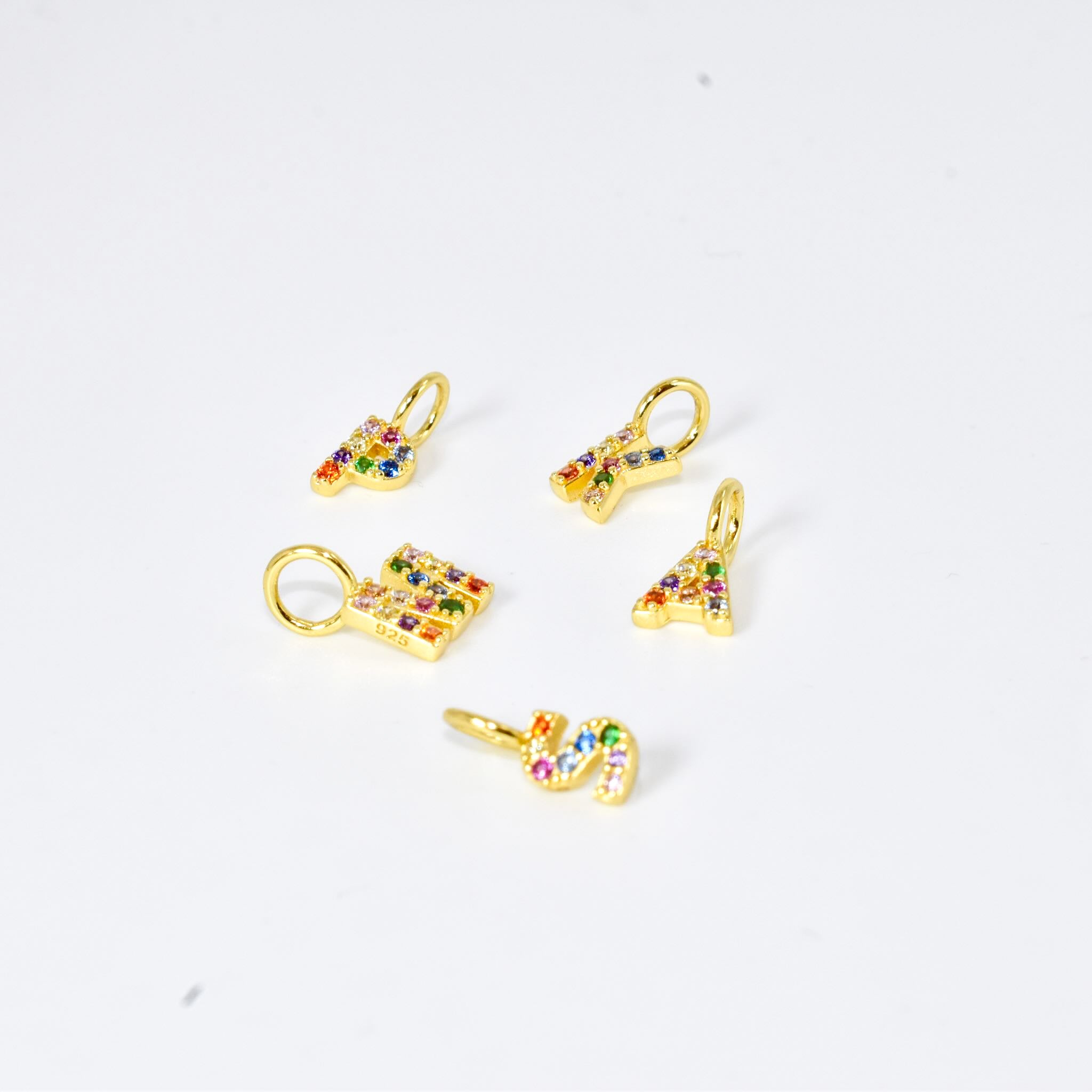 Set of gold initial letter pendants with colorful stones on a white background