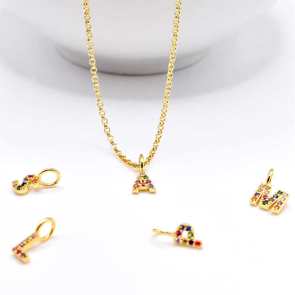 Gold initial necklace hanging with multiple pendants with colorful gemstones on a white background