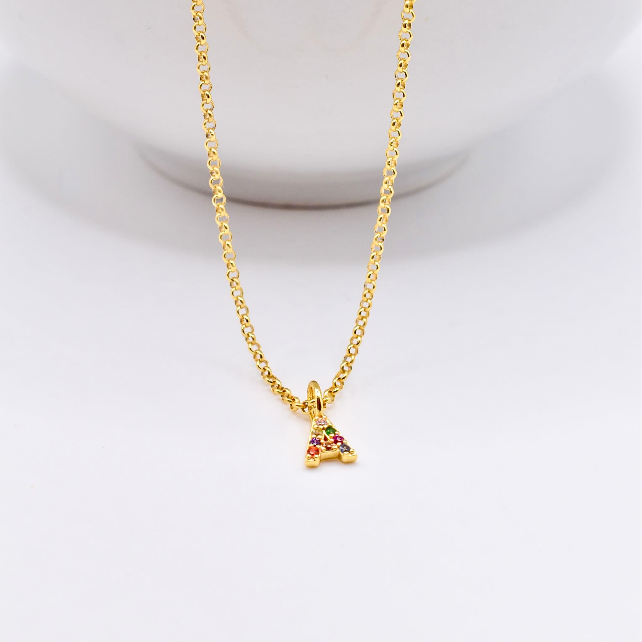 Gold necklace with a initial pendant A with coloured stones hanging on white background