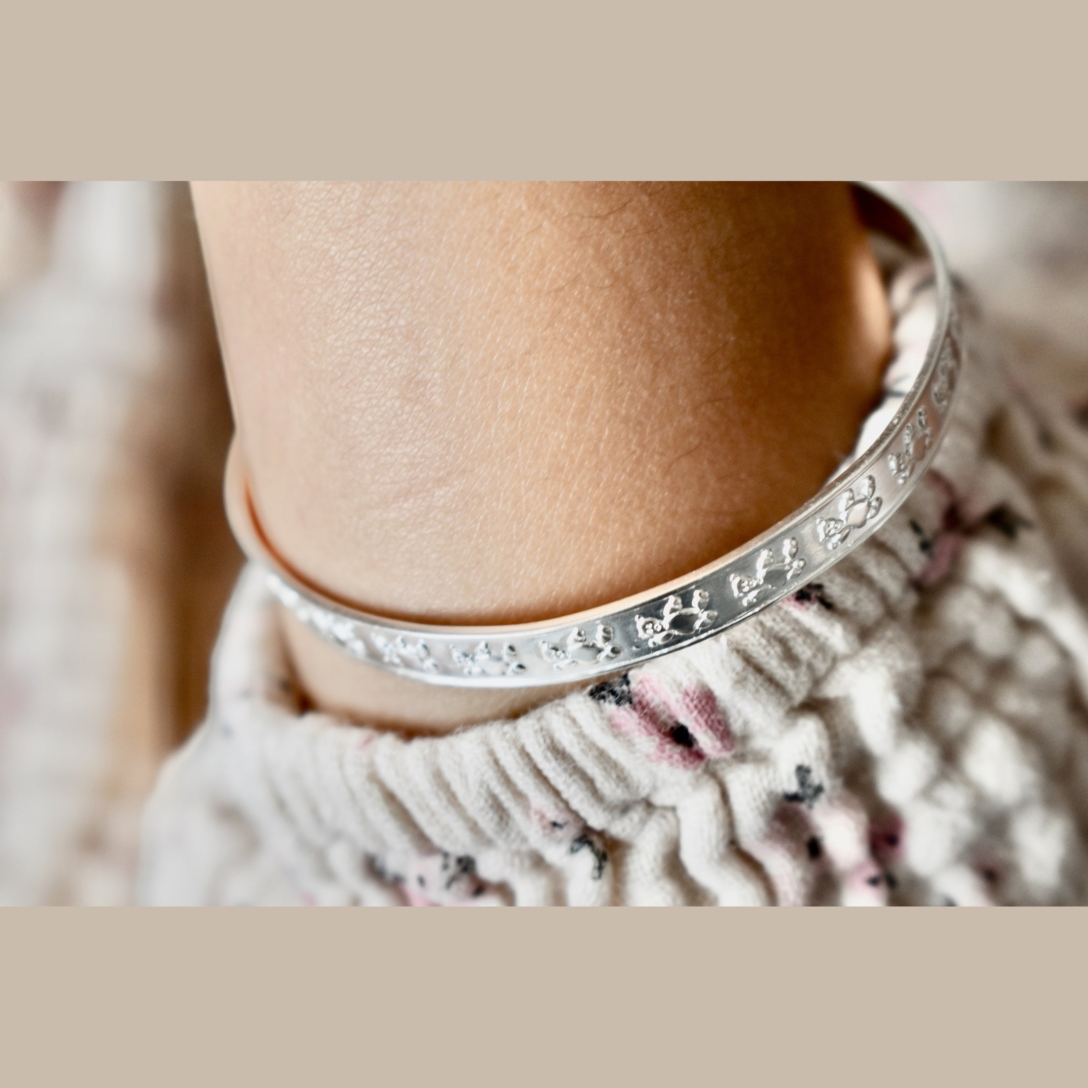 Silver bracelet with floral patterns on a wrist against a neutral background