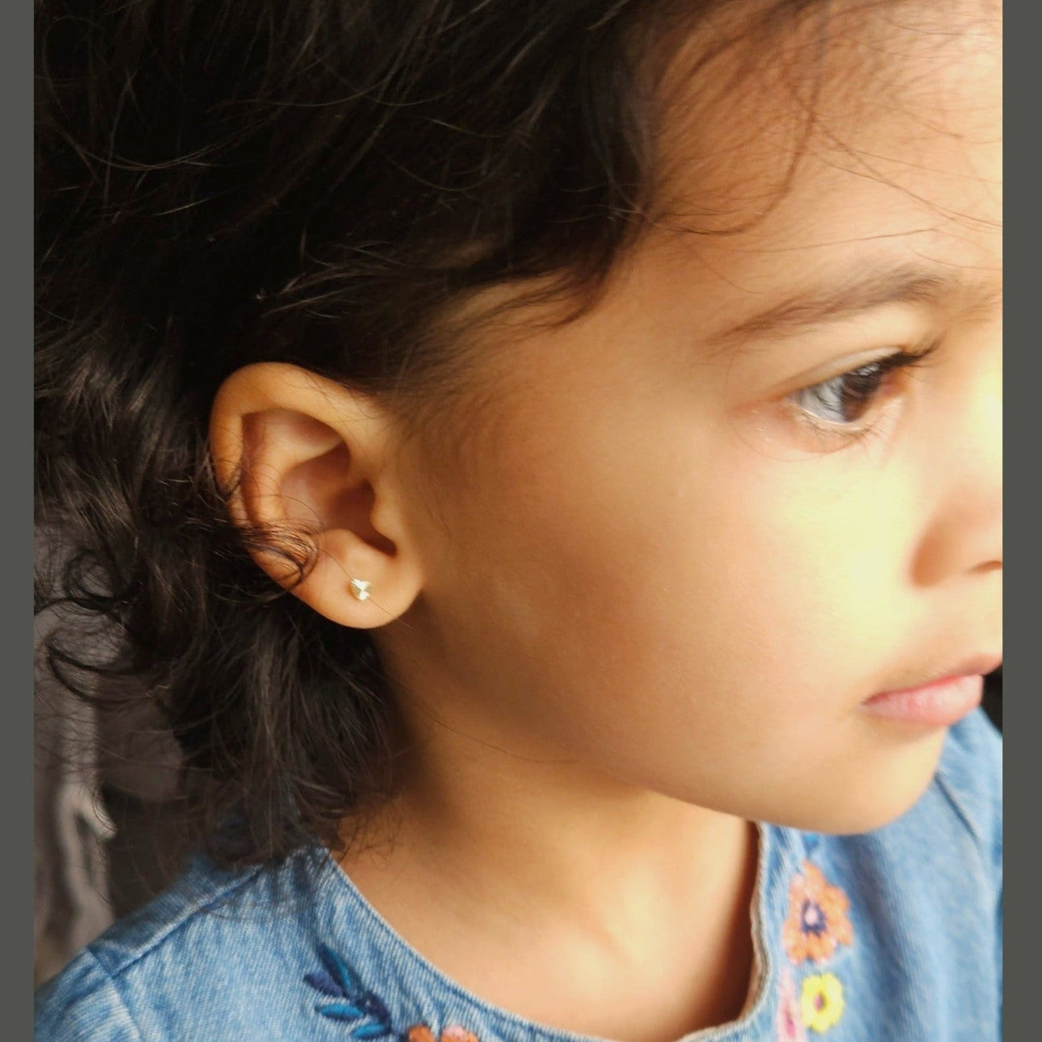 gold heart stud earrings in girl's ear in blue dress