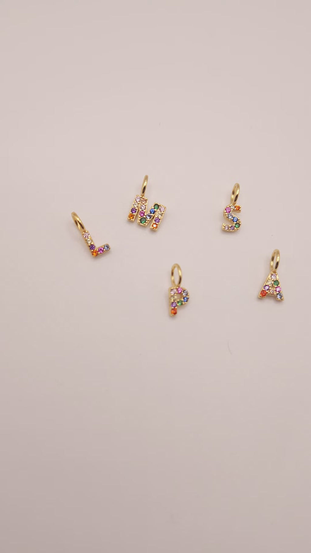 Video of Rainbow initial pendants laying on cream colour background 