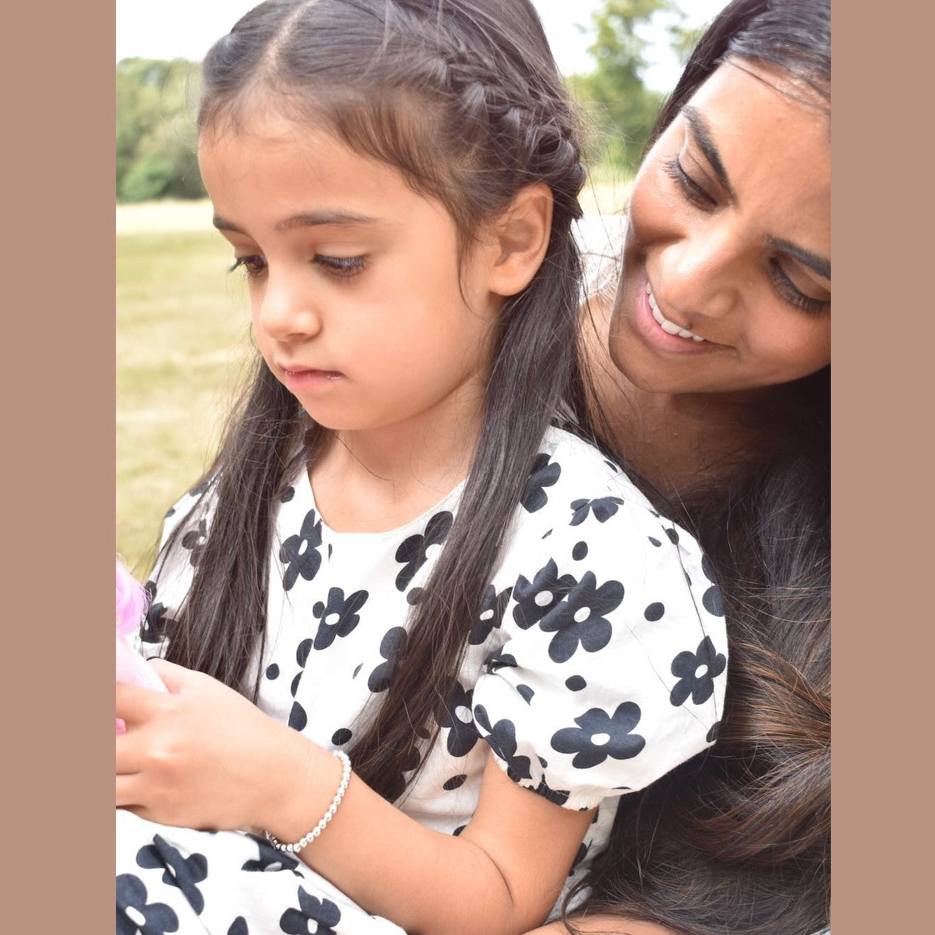 Woman and young girl sitting together outdoors, smiling.